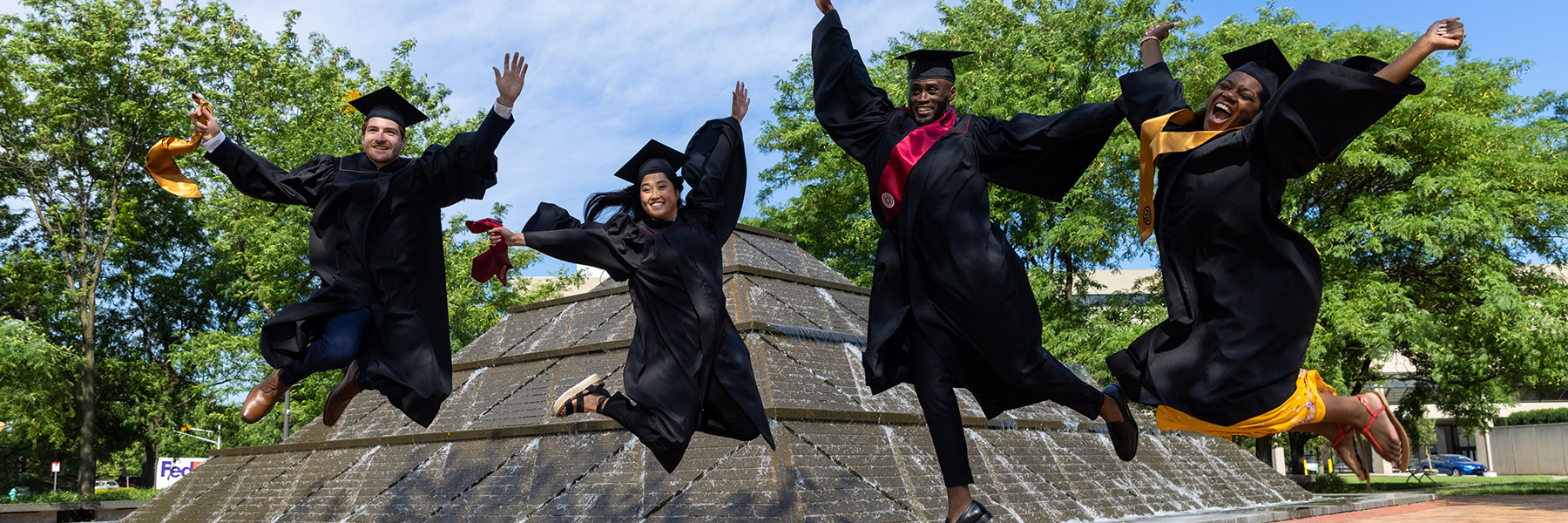 graduates jumping in front of wood fountain